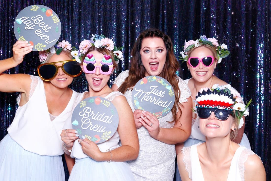 Bride and bridal party enjoying a wedding photo booth with fun props and signs