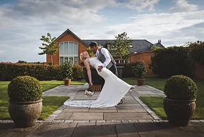 A bride and groom sharing a romantic dip kiss in the sunny courtyard at Cider Mill Barns wedding venue, with the main barn in the background.
