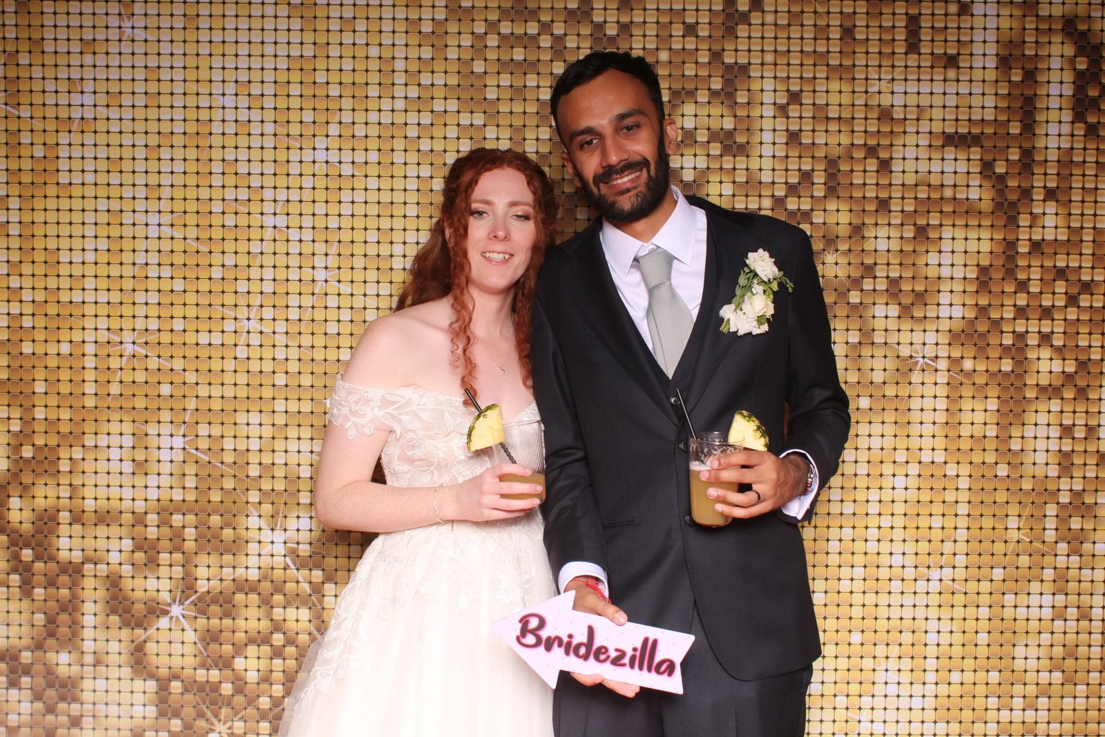 Bride and groom holding props in front of a gold shimmer sequin backdrop